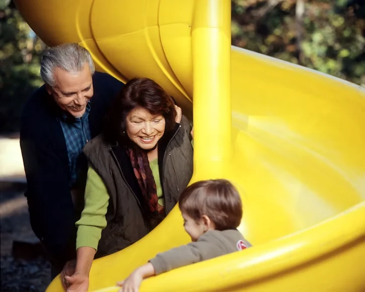 Grandparents watching their toddler grandchild on a slide