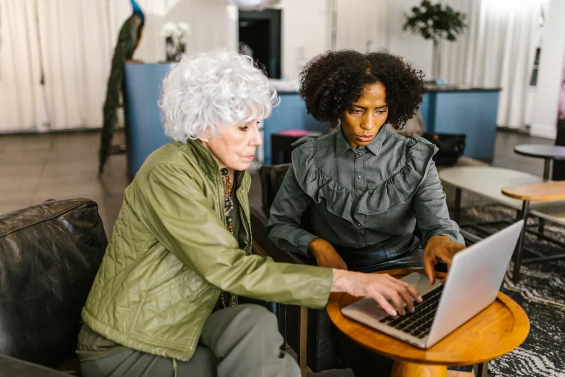 Two women working together on a laptop in a modern office setting.