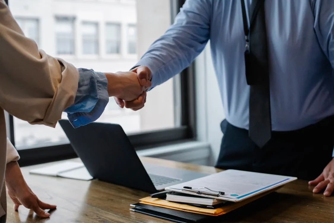 Retiree and financial planner shaking hands in a modern office setting.