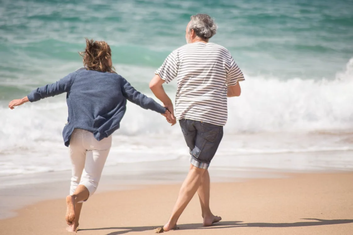 Senior couple holding hands and running by the ocean at a Florida beach during the day.