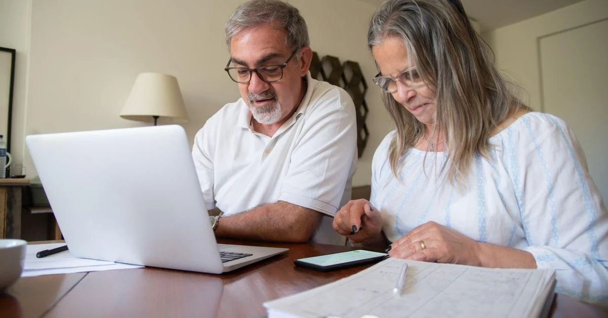 Senior couple working together on retirement income planning documents with a laptop and phone at home