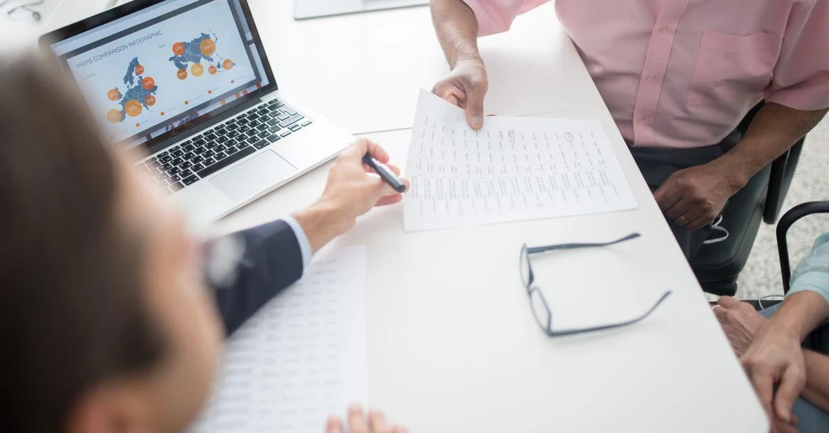 Senior couple reviewing insurance documents with a consultant at an office desk with a laptop