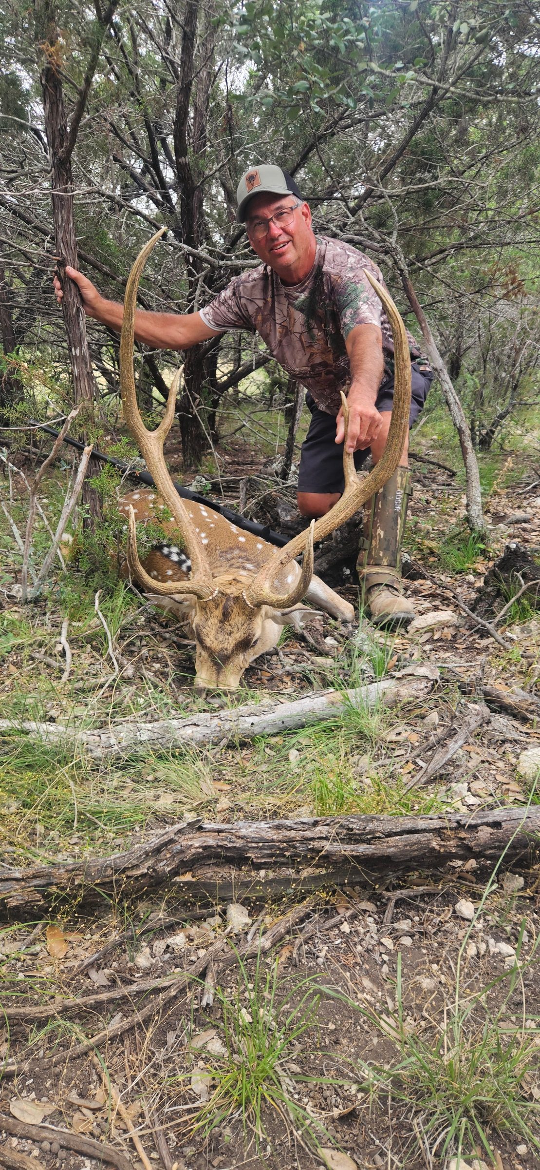 Hunter with a harvested axis buck in cedar cover at FF Hunting Ranch in June 2026