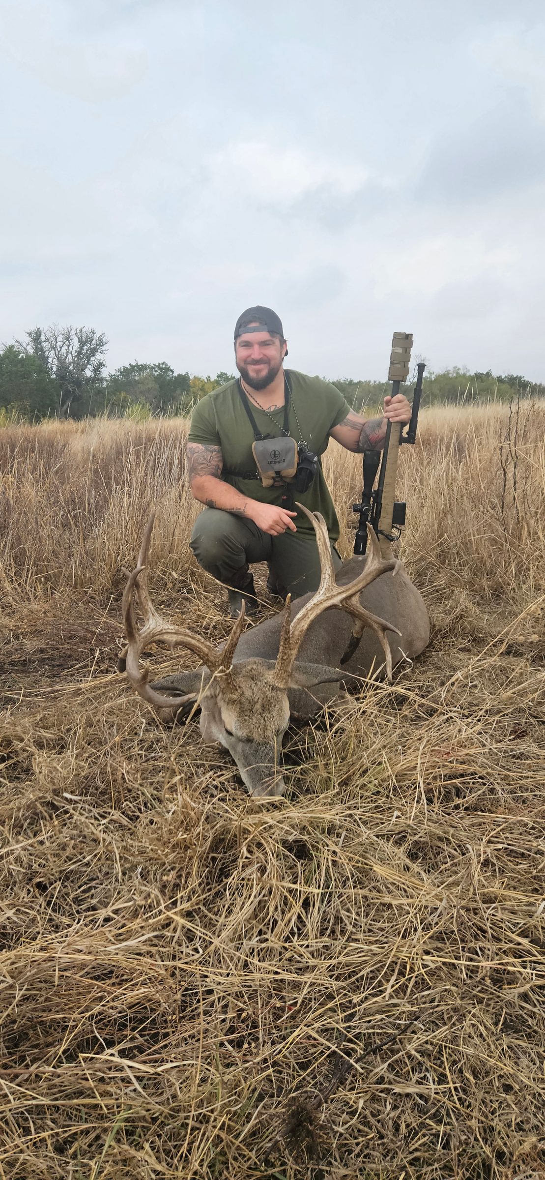 Hunter with a harvested whitetail buck in open grass at FF Hunting Ranch